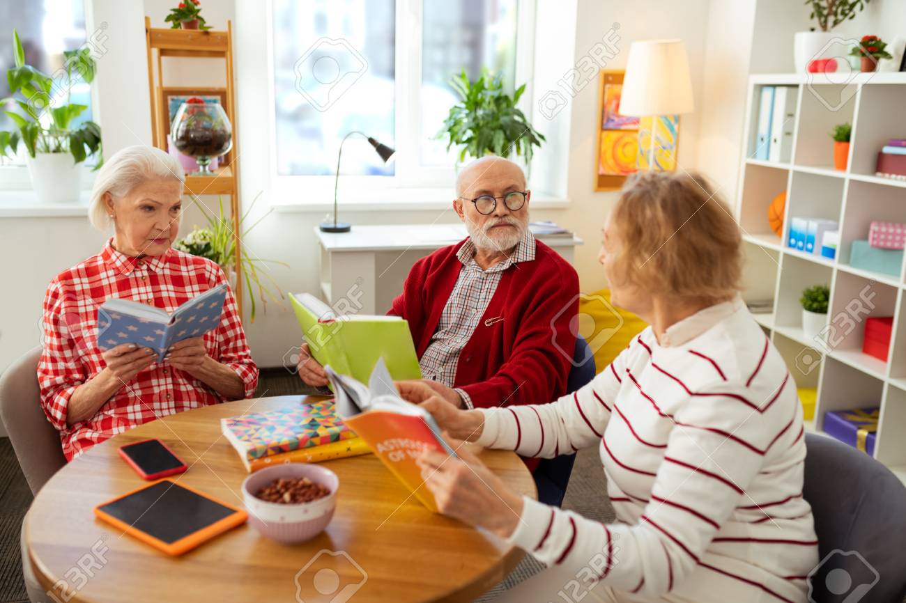 Sharing information. Nice senior people speaking about different books while sitting around the table